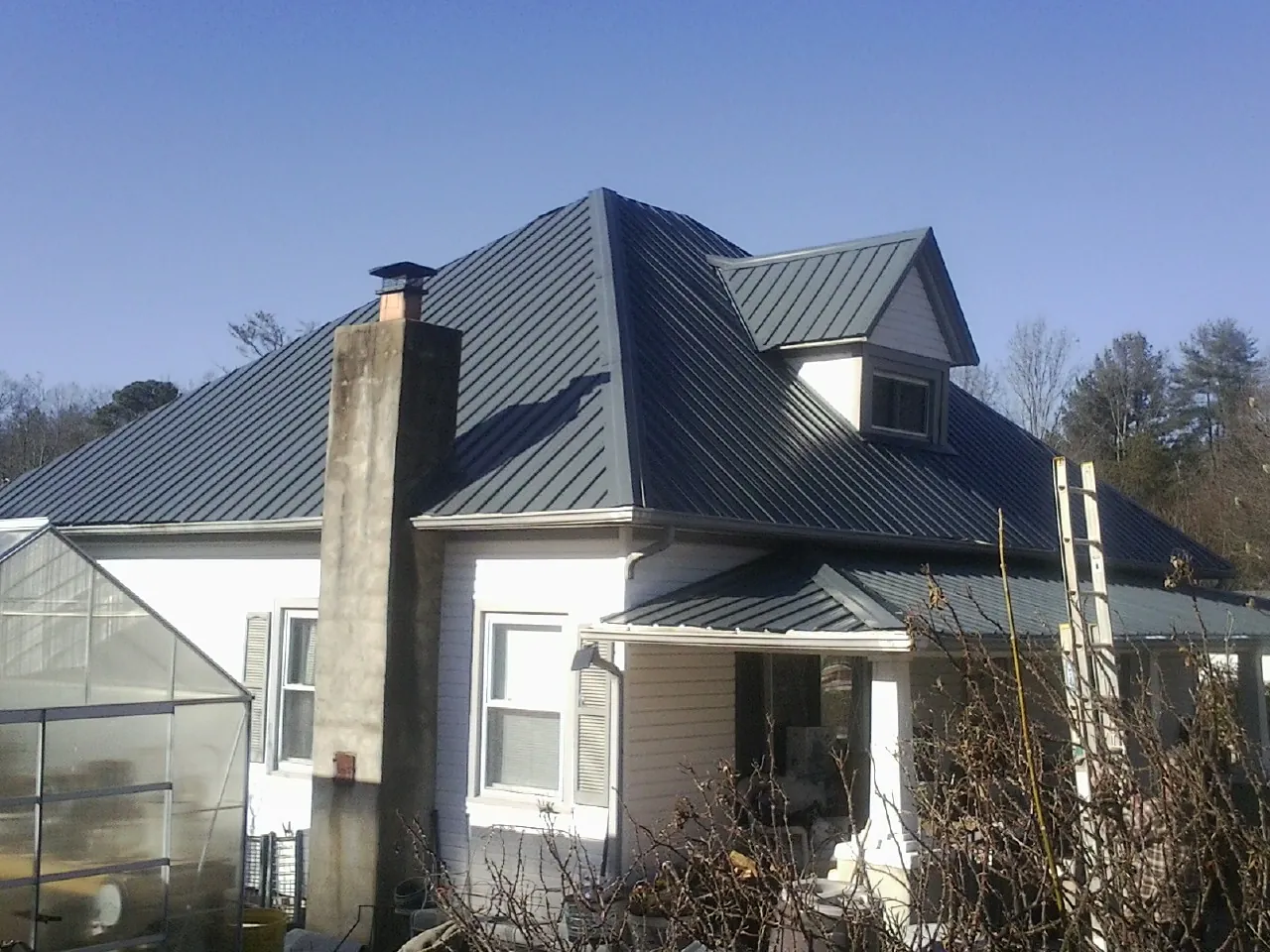 Dark blue standing seam metal roof on a white farmhouse with dormer — Slate & Tile Roof Repair by Roofing Brothers in Batson