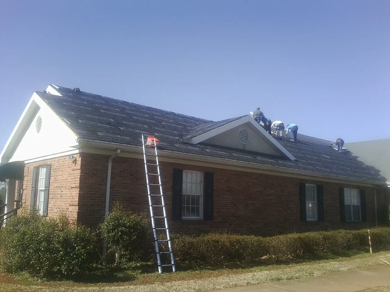 Crew tearing shingles off a brick ranch roof with a ladder set — Metal Roof Repair work by our crew in Batson