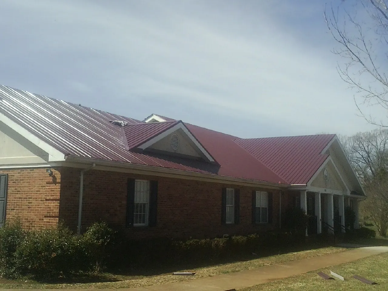 Red metal roof with gabled entries on a long brick building, from a Hail Damage Roof Repair job in Batson