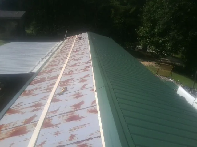 Old rusted panels beside newly installed green metal roofing — Wind Damage Roof Repair by Roofing Brothers in Batson
