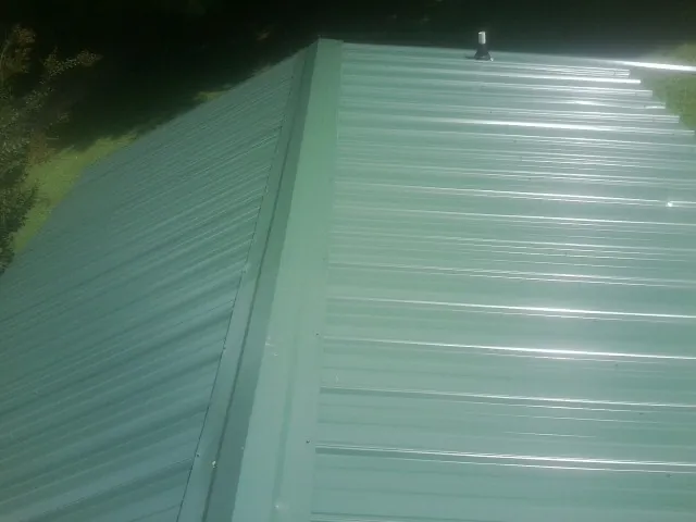 New green metal panels meeting at the ridge of a roof — Flat Roof Repair work by our crew in Batson