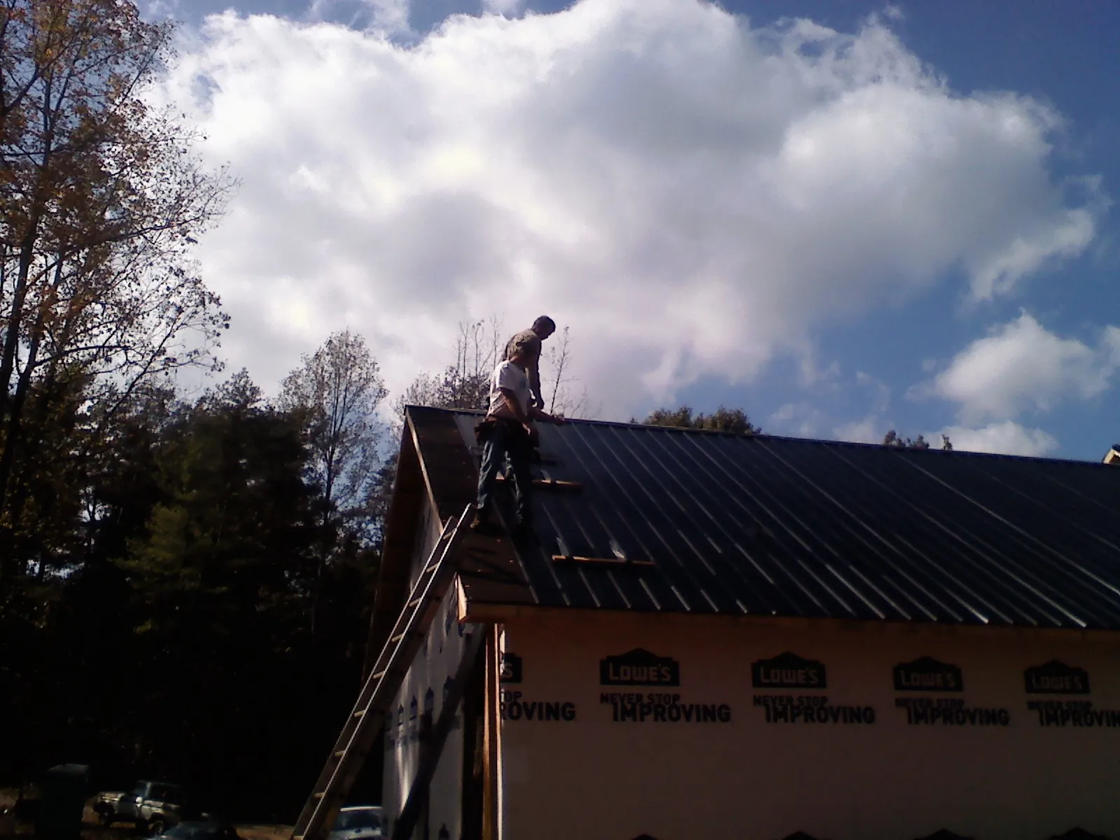 Roofer fastening dark metal panels high against a cloudy sky, from a Roof Inspection job in Batson