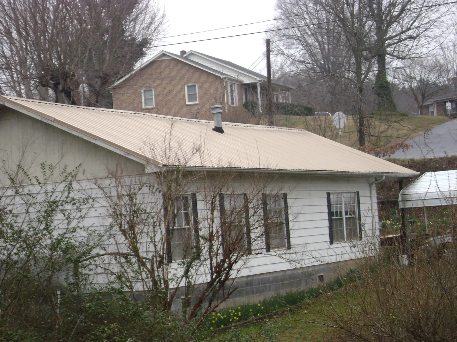 Tan metal roof on a white sided house set into a hillside — Commercial Roofing by Roofing Brothers in Batson
