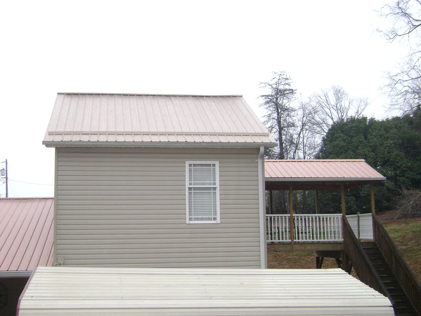 Tan metal roofs on a two story addition and attached porch, from a Roof Replacement job in Batson